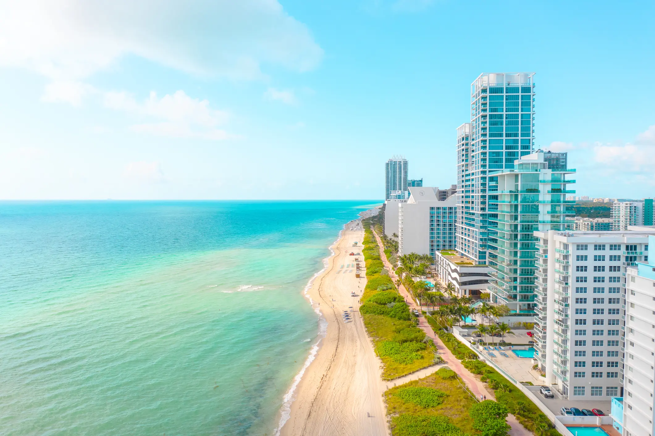 From a Miami high-rise, catch the ocean's serene left, lush trees, and busy roads leading to city buildings under a clouded sky—a picturesque scene for a vacation rental.