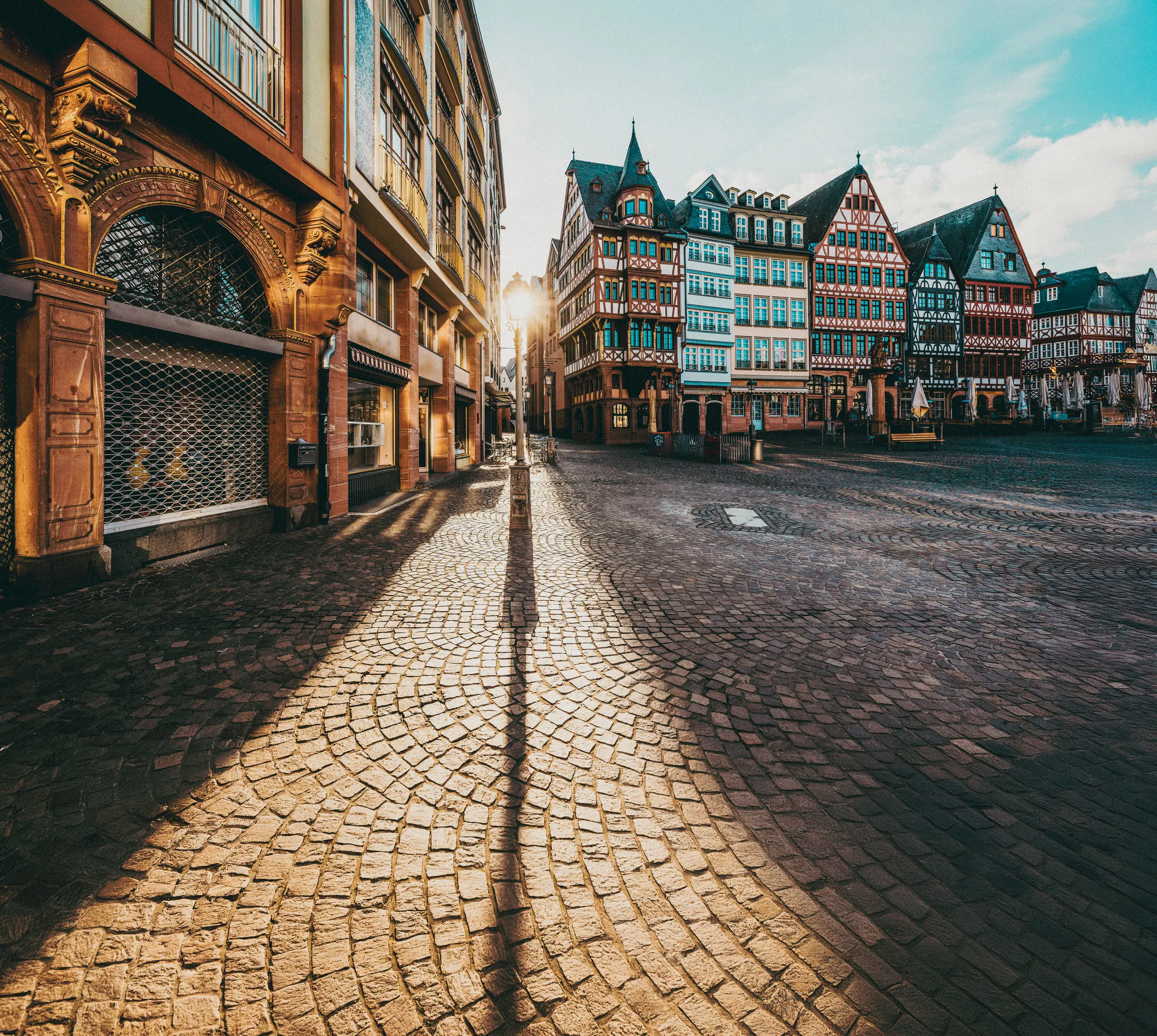 Frankfurt's charm mirrors that of Heidelberg, with cobblestone streets and historic buildings. Windows and light poles add to the scene, set against a cloudy sky, boasting a picturesque old-town vibe.