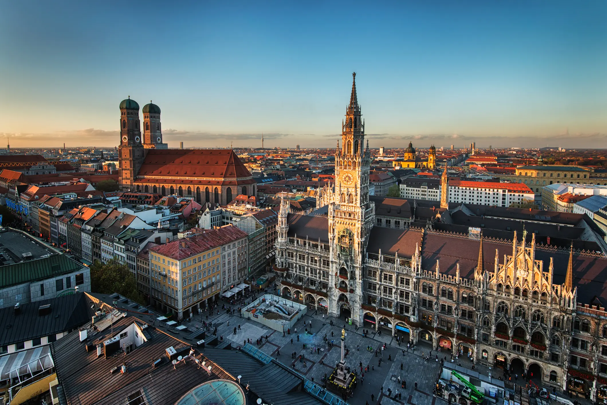 Munich, Germany is depicted with bustling streets filled with people and vehicles, surrounded by buildings and lush trees, all under a vibrant blue sky—a quintessential urban scene.