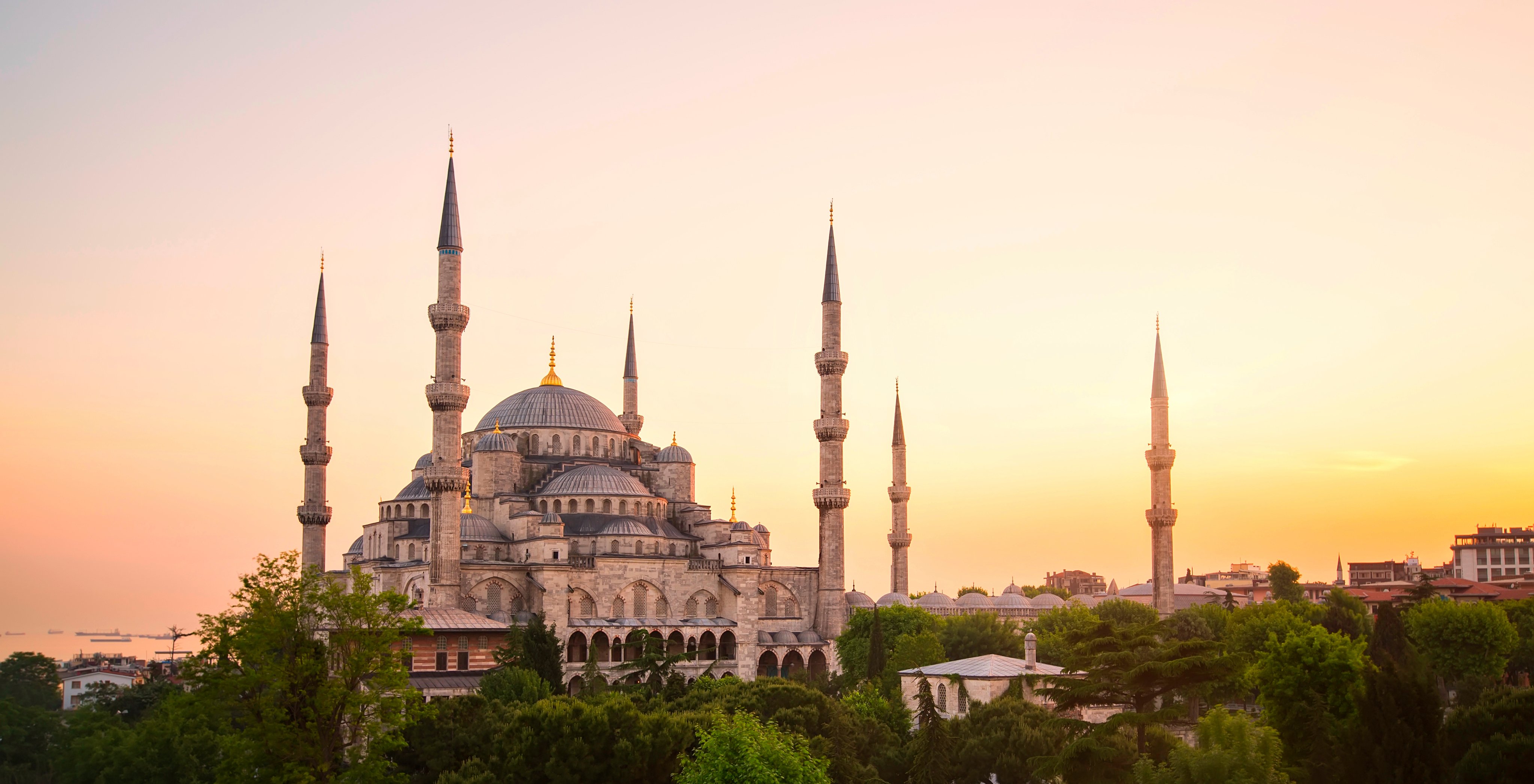 In Istanbul, the iconic Blue Mosque stands majestically, framed by lush trees and nearby buildings, all under a stunning sky that completes this breathtaking scene.