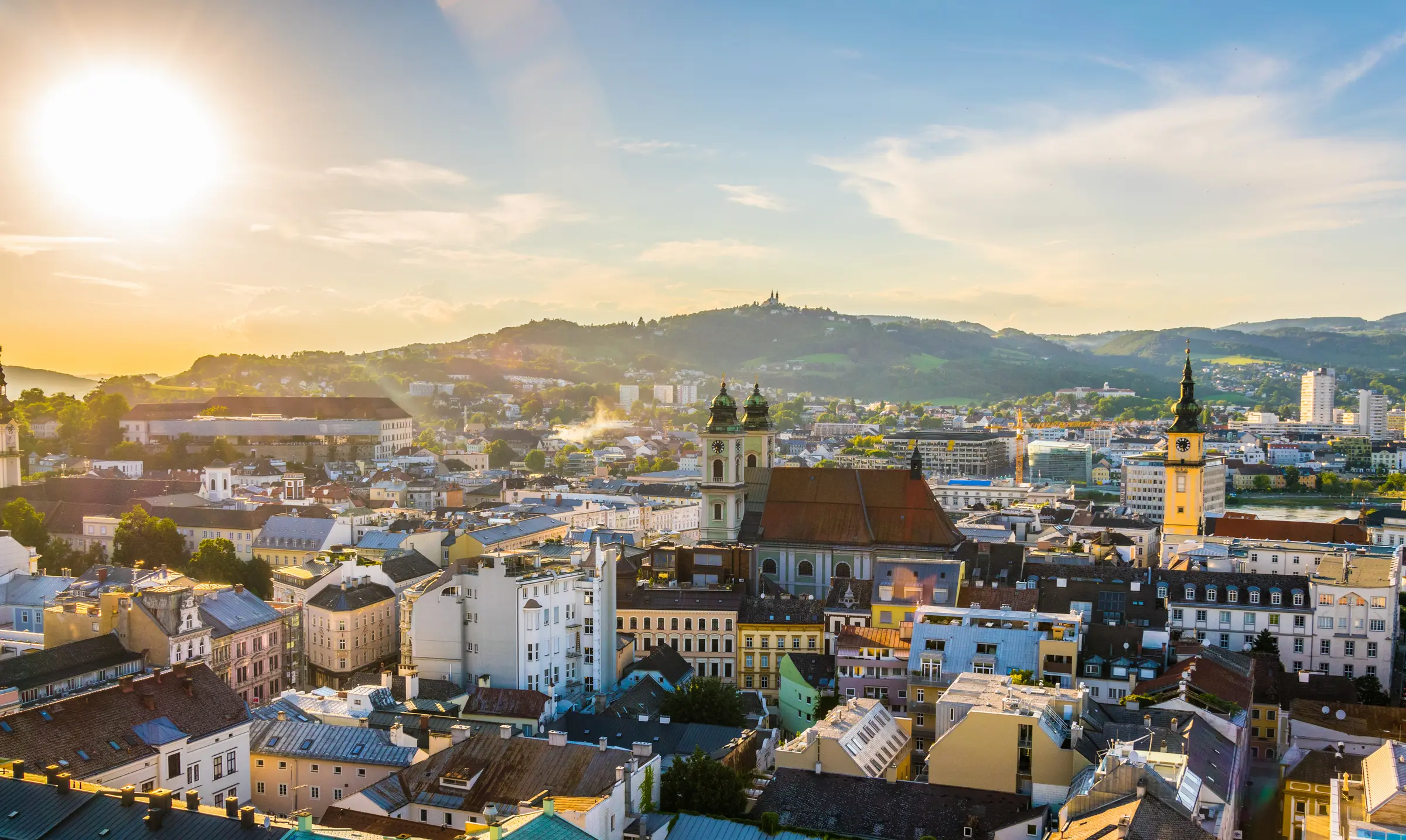 Linz embraces the sunset aura, reminiscent of Ljubljana, with its urban landscape aglow. Buildings, houses, and nature harmonize under the warm embrace of twilight, painting a picturesque skyline.