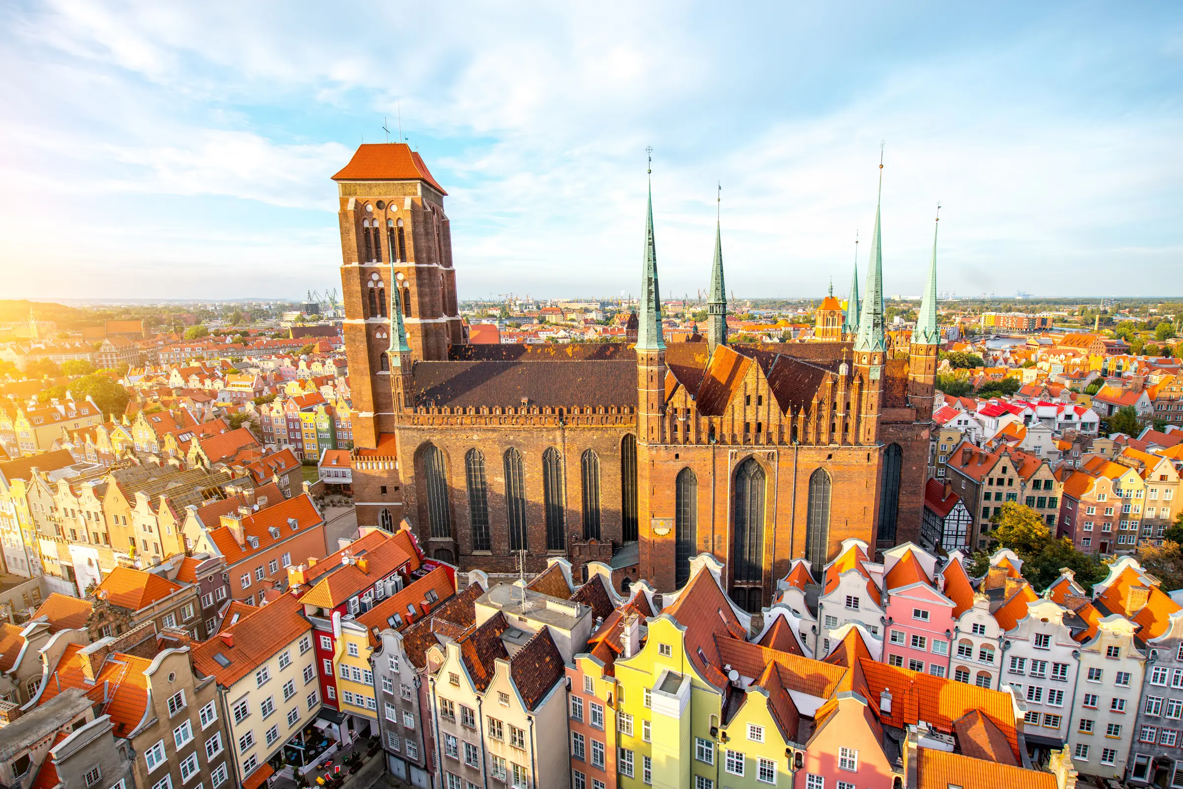 Gdańsk's old town in Poland boasts charming houses, historic buildings, and lush trees. Vehicles hum along under a cloud-filled sky, creating an idyllic setting perfect for a European vacation.