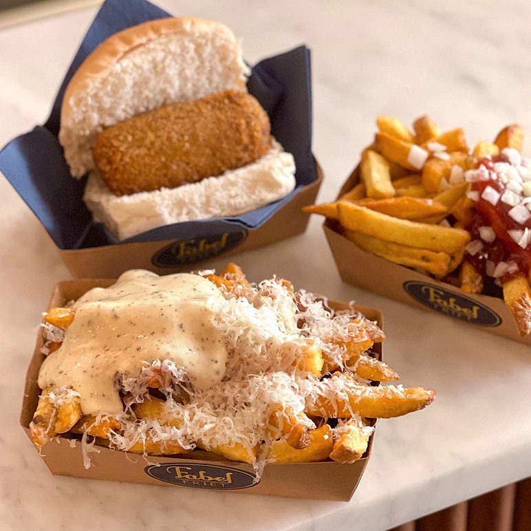 Close-up of two dishes of French fries and a frikandel in a bun