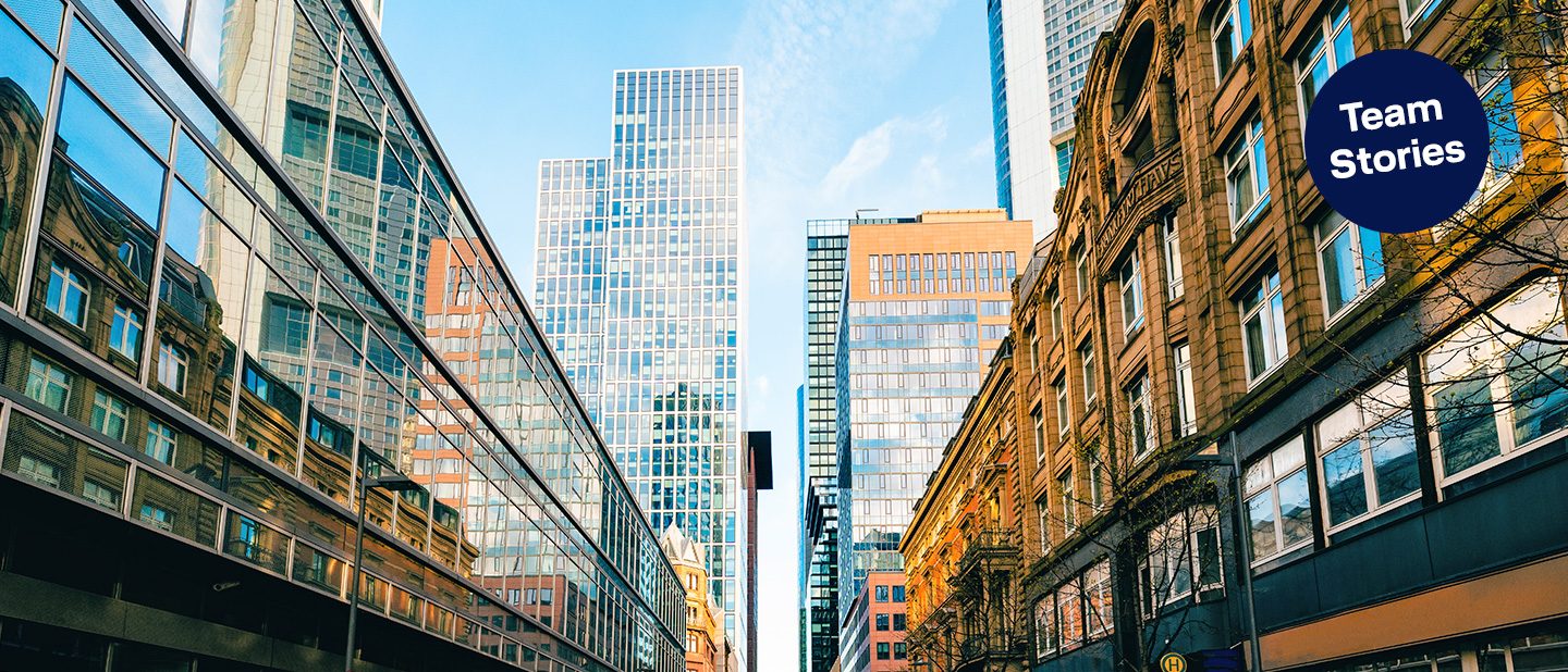 Team Stories: Blick durch eine Häuserschlucht in Frankfurt auf Hochhäuser und blauen Himmel.