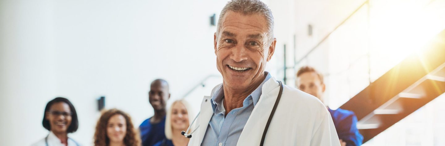 L&radic;&sect;chelnder Arzt im Krankenhaus mit Assistenz&radic;&sect;rzten // Smiling doctor standing in a hospital with his staff