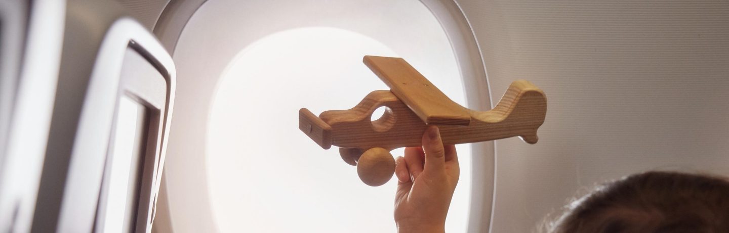 Junge spielt mit Holzflugzeug im Flugzeug. // Boy playing with wooden airplane in an airplane.