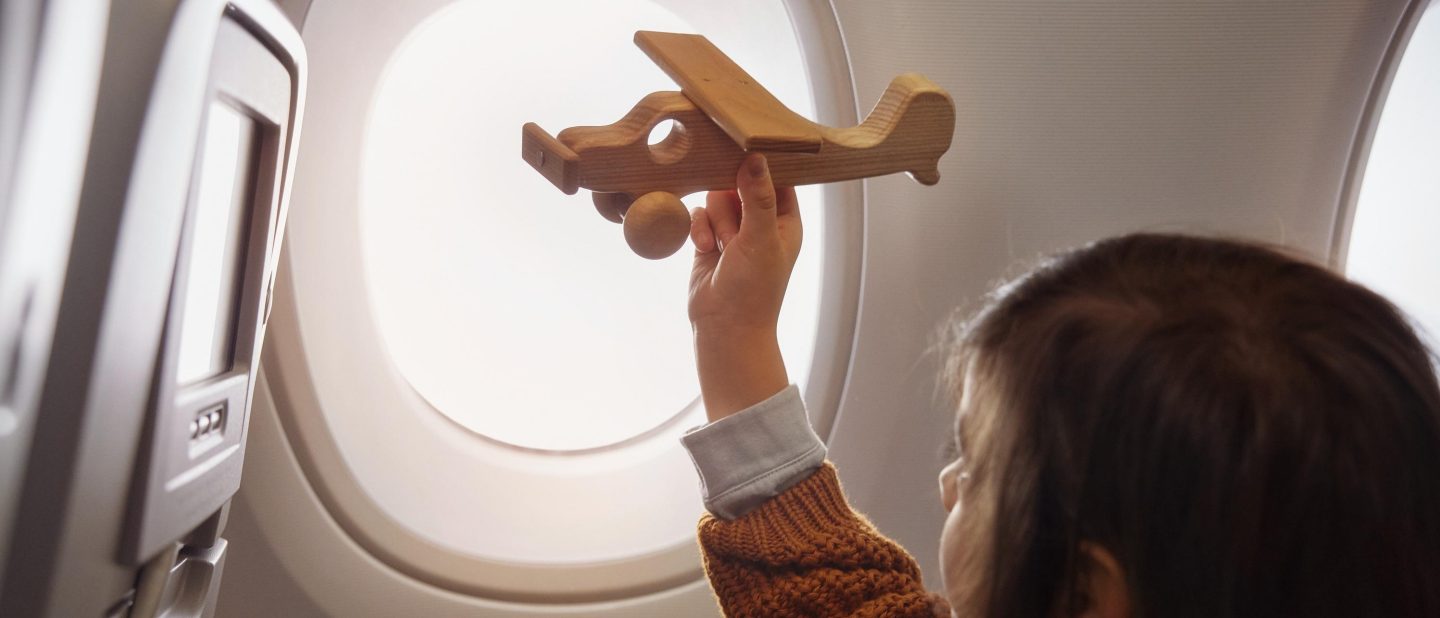 Junge spielt mit Holzflugzeug im Flugzeug. // Boy playing with wooden airplane in an airplane.