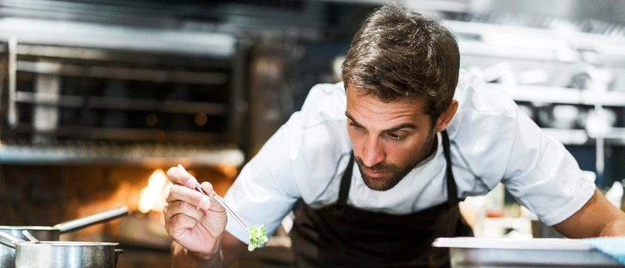 Concentrated chef garnishing food. Male cook is preparing dish in commercial kitchen. He is working in restaurant.