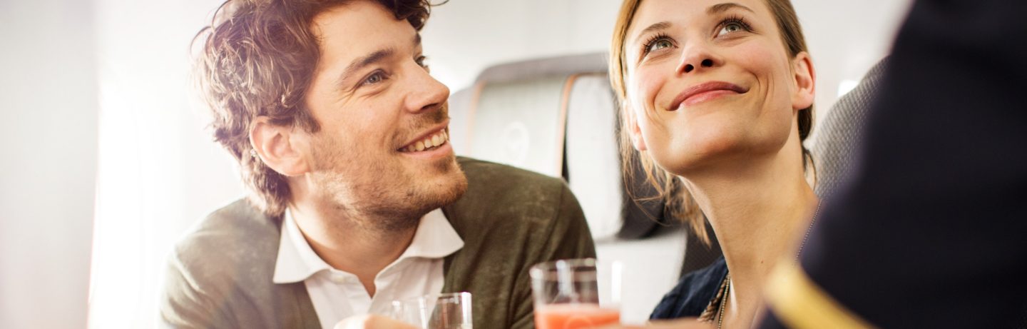 junges Paar bekommt Welcome Drink in Premium Economy Class serviert//young couple gets welcome drink in Premium Economy Class