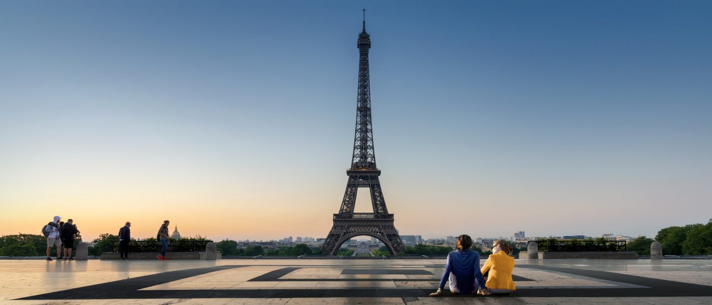 Paris, Frankreich: Sitzendes Paar blickt auf den Eiffelturm bei Abendd&auml;mmerung. // Paris, France: Sitting couple looking up at the Eiffel Tower at dusk.