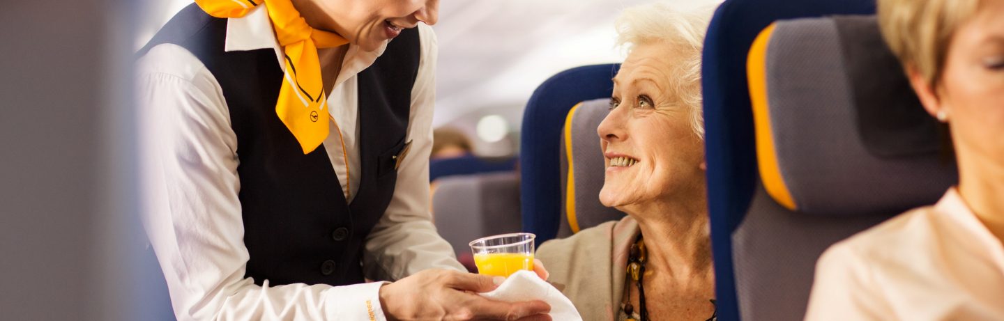 Eine Flugbegleiterin serviert einen Orangensaft. // A flight attendant is serving an orange juice.