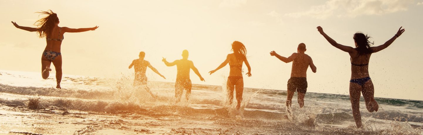 Silhouettes of happy friends runs at sunset sea beach. Beach vacations concept