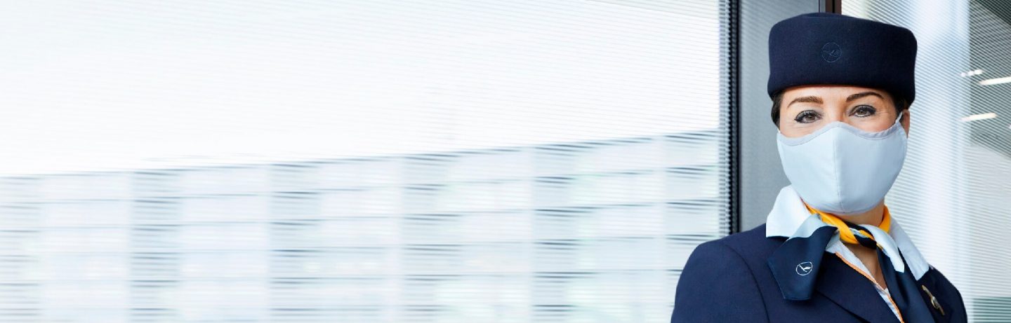 Airport: Lufthansa employee with a mask in front of a window at the airport. // Flughafen: Lufthansa Mitarbeiterin mit Maske vor Fensterfl&auml;che am Flughafen.